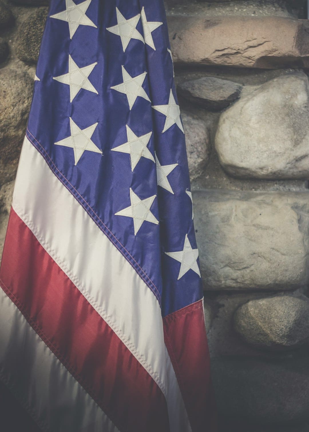 An American flag honoring our Veterans hangs draped from a pole against a stone backdrop.